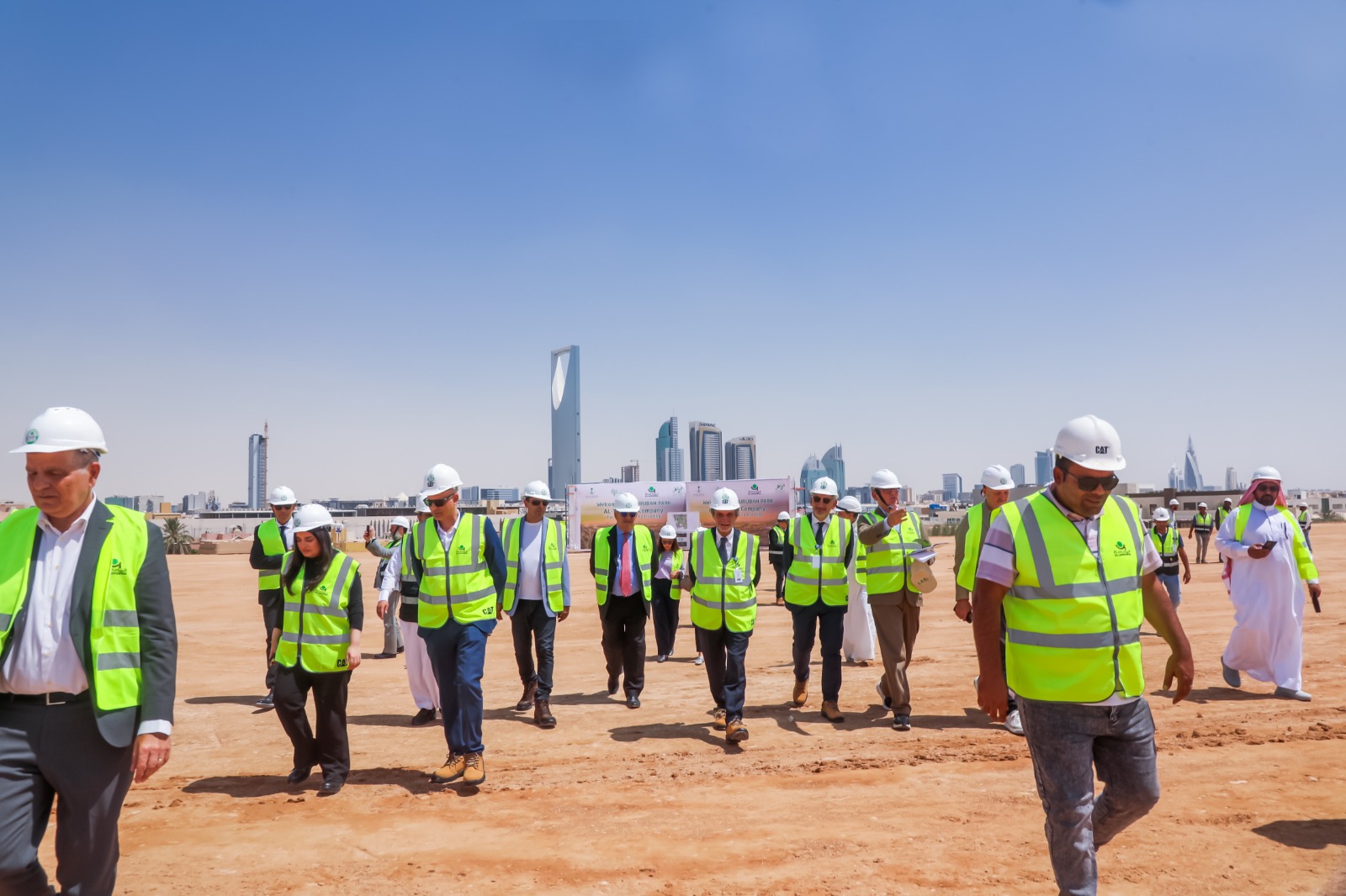 A group of people with construction site attire on a sandy site with Riyadh's skyline in the background