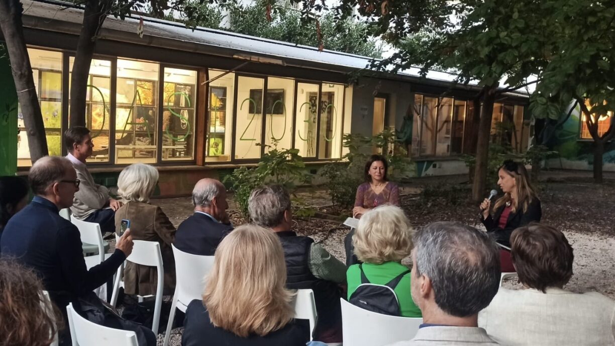 People on chairs in a garden, evening, listening to two female speakers