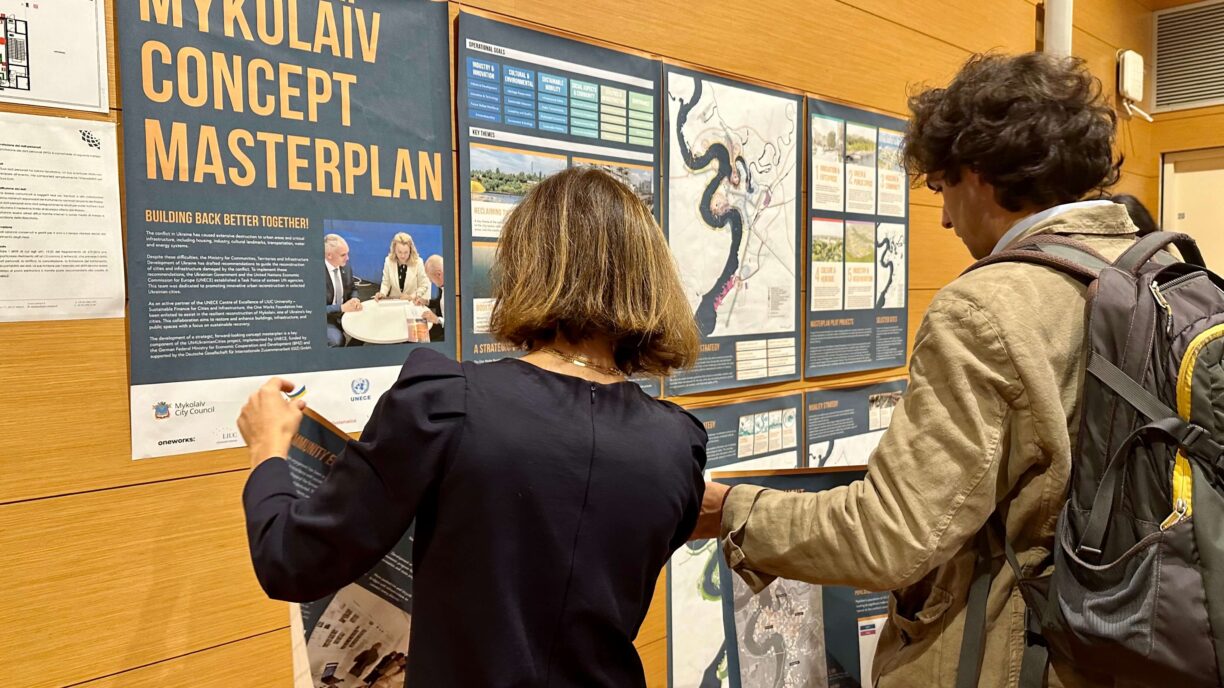 A woman and a man in front of a poster regarding the reconstruction of Mykolayev in Ukraina