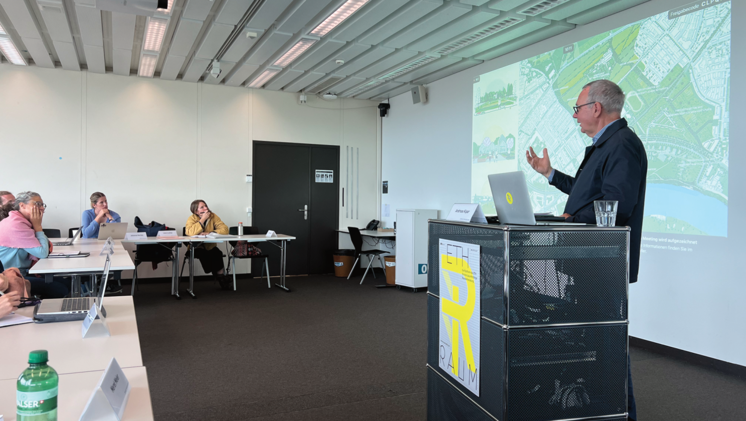 A man standing in front of a class room with students and a Power Point Presentation in the background